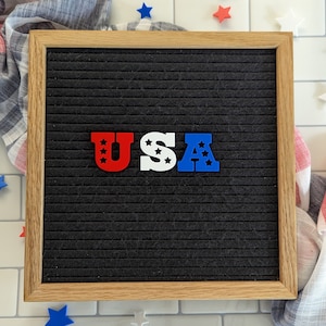 May include: A black letter board with a wooden frame, spelling out "USA" in red, white, and blue letters. The letters are decorated with small white stars.