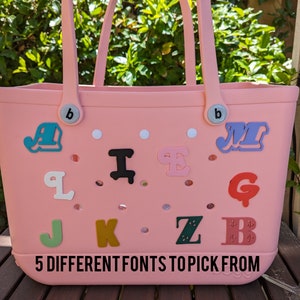 May include: A pink tote bag with a variety of colourful letters attached to it. The letters are in different fonts and styles. The text on the bag reads "5 DIFFERENT FONTS TO PICK FROM".