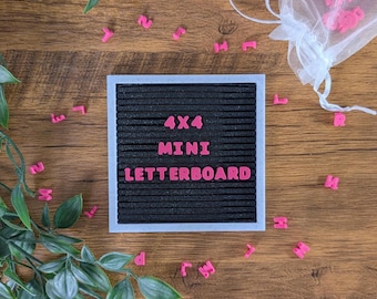 May include: A black 4x4 mini letterboard with pink letters spelling "4x4 MINI LETTERBOARD" on a wooden surface with pink letter tiles scattered around it.