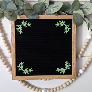 May include: A black letter board with a wooden frame. The board has green leaf-shaped decorations in each corner.