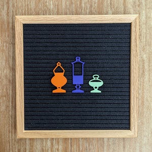 May include: Three decorative, cutout, metal ornaments in the shape of vases. The vase on the left is orange, the middle vase is blue, and the vase on the right is green.