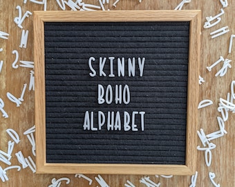 May include: A black felt letter board with a wooden frame. The board displays the text "SKINNY BOHO ALPHABET" in white plastic letters.