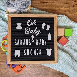 Peut inclure: Un tableau d'affichage noir avec des lettres blanches qui &eacute;pellent "Oh Baby Sarah's Baby Shower". Le tableau est d&eacute;cor&eacute; de d&eacute;coupes en feutre blanc d'un ours en peluche, d'un biberon, d'une &eacute;toile, d'une sucette et d'une paire de pieds de b&eacute;b&eacute;. Le tableau est pos&eacute; sur une surface en bois avec une couverture bleue et blanche et quelques blocs de bois color&eacute;s.