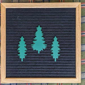 May include: Three green felt cutouts of pine trees on a black felt letter board with a wood frame.