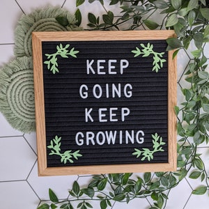 May include: A black letter board with a white wooden frame and green leaf accents. The board displays the message "KEEP GOING KEEP GROWING".