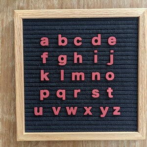 May include: A black felt letter board with a wooden frame. The letters of the alphabet are displayed in red on the board.