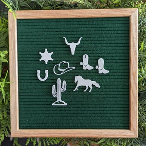 May include: A green felt letter board with white felt cutouts of western themed icons, including a sheriff's star, a horseshoe, a cowboy hat, a cactus, a bull's head, a horse, and two pairs of cowboy boots.