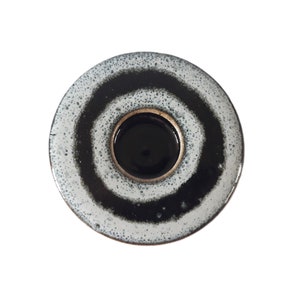 May include: A white ceramic saucer with black concentric circles and a black centre hole.