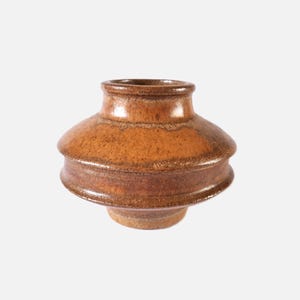 May include: A small, brown ceramic vase with a rounded, slightly flared base and a narrow opening. The vase has a textured, speckled glaze with shades of brown and orange.