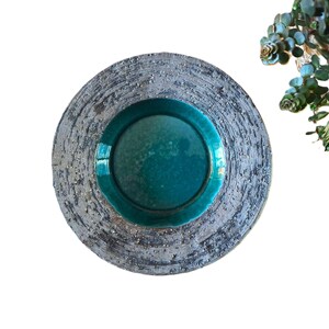 Peut inclure: Une assiette en céramique artisanale avec un centre turquoise et un anneau extérieur gris texturé. L'assiette a un aspect rustique et artisanal, parfaite pour servir des aliments ou comme pièce décorative. Le diamètre de l'assiette est d'environ 30 cm.