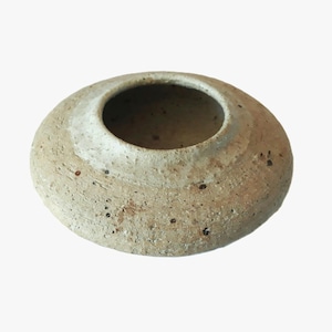 May include: A beige ceramic bowl with a wide, shallow design and a central opening. The bowl has a textured surface with small, dark speckles, and a lighter-colored rim. The overall shape is round and low, suitable for decorative or functional use.