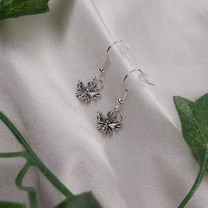 May include: A pair of silver bee dangle earrings. The bees are detailed and have a textured finish.
