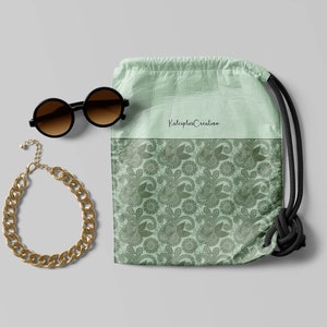 May include: A green drawstring bag with a paisley pattern and the text "Kaleidoscope Creation". The bag is next to a pair of round sunglasses and a gold chain necklace.