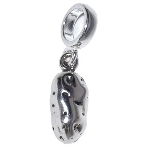May include: A silver-colored charm in the shape of a potato. The charm has a loop at the top for attaching to a bracelet or necklace. The potato charm has a textured surface with small, dark spots.