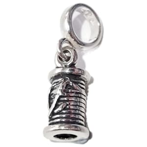 May include: A silver-colored charm featuring a spool of thread with a needle design. The charm has a loop at the top for attaching to a bracelet or necklace. The spool is detailed with horizontal lines and a decorative element.