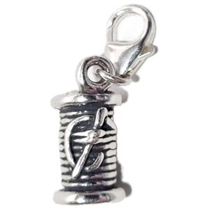 May include: A silver-colored charm featuring a spool of thread with a needle and thread design. The charm has a lobster clasp for easy attachment to a bracelet or necklace. The charm is a sewing-themed accessory.