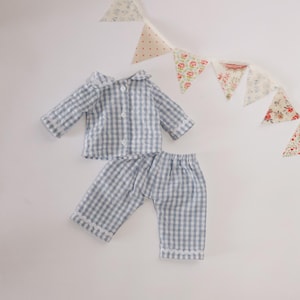 May include: A blue and white checked pyjama set, comprising a collared shirt and trousers. The set is displayed on a white background, with a decorative garland of floral and polka dot fabric triangles.