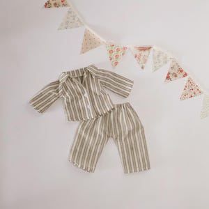 Pode incluir: Um conjunto de pijama em miniatura com um padr&atilde;o listrado em tons de bege e castanho. O conjunto inclui uma camisa com bot&otilde;es e cal&ccedil;as a condizer. Uma grinalda de tri&acirc;ngulos de tecido com estampados florais e de bolinhas est&aacute; pendurada por cima.