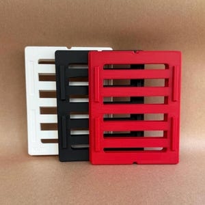 May include: Three rectangular, slotted grid trays in white, black, and red. Each tray features a series of horizontal cutouts and raised vertical side rails. The trays are stacked slightly offset, displaying their uniform design and matte finish.