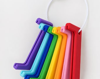 May include: A set of eight L-shaped plastic stands in a rainbow color gradient, including purple, light blue, dark blue, green, yellow, orange, pink, and red, all held together by a white circular metal cable with a screw-top connector.