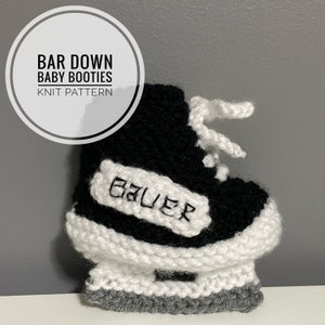 May include: Black and white knitted baby booties shaped like ice skates. The booties have a white "Bauer" logo on the side.