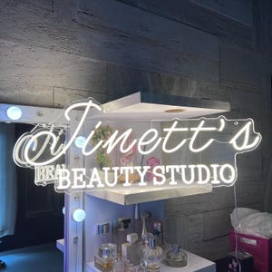 May include: White neon sign with the text "Jinett's Beauty Studio" on a white wall.