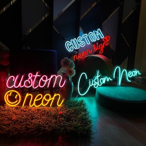May include: Three neon signs with the text "Custom Neon", "Custom neon sign" and "custom neon" with a smiley face. The signs are pink, blue and yellow.
