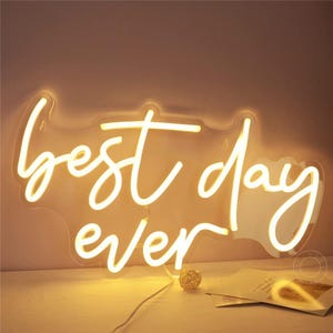 Puede incluir: Un letrero de neón blanco con las palabras "best day ever" en una fuente cursiva. El letrero está iluminado y brillando.