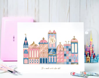 May include: A white card with a pink, blue, and gold illustration of the "it's a small world" ride at Disneyland. The text "It's a small world after all!" is printed below the illustration.