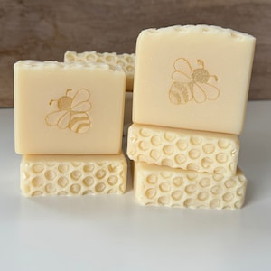 May include: Four bars of honey soap with a honeycomb design and a bee graphic. The soap is a light yellow color.