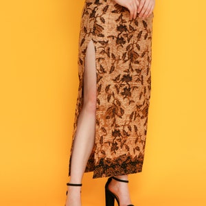 May include: A long brown skirt with a black floral pattern and a side slit. The skirt is worn with black heeled sandals.