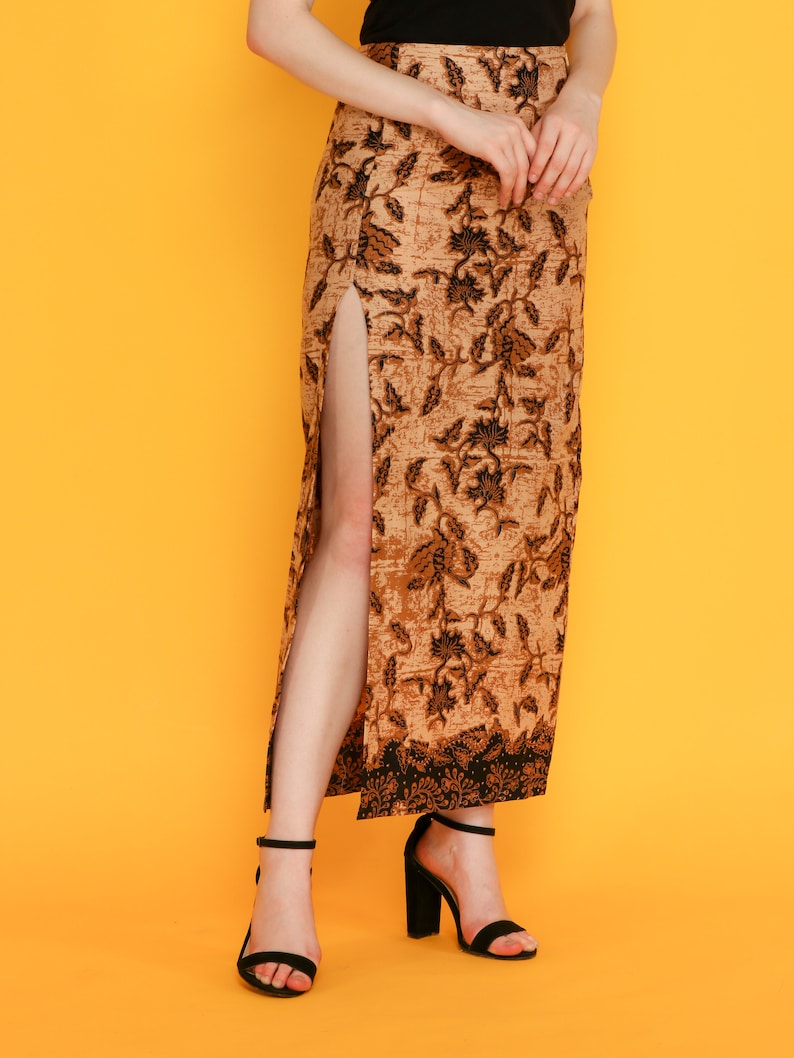 May include: A long brown skirt with a black floral pattern and a side slit. The skirt is worn with black heeled sandals.