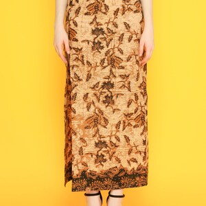 May include: A long brown skirt with a black floral pattern. The skirt has a slit on the side and a black waistband.