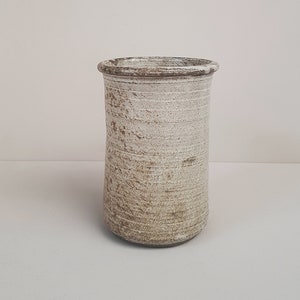 May include: A white ceramic vase with a brown glaze. The vase has a cylindrical shape and a slightly flared rim.