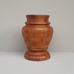 May include: A wooden vase with a checkered pattern. The vase is brown and has a round base.