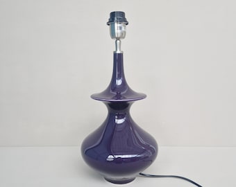 May include: A purple ceramic table lamp with a simple design. The lamp has a round base and a tall, slender neck.