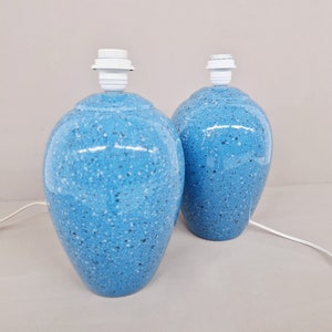 Puede incluir: Dos lámparas de mesa de cerámica azul moteada con portalámparas blancos. Las lámparas tienen forma redondeada, como de jarrón, y están conectadas a un cable eléctrico blanco. Las lámparas son de color azul claro con motas azules oscuras y blancas.