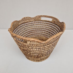 May include: A woven wicker basket with a scalloped rim and two handles. The basket is made of natural brown wicker and has a light brown color.