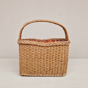 May include: A woven wicker basket with a single handle. The basket has a rectangular shape and a brown, natural color. The inside of the basket is lined with a floral patterned fabric.