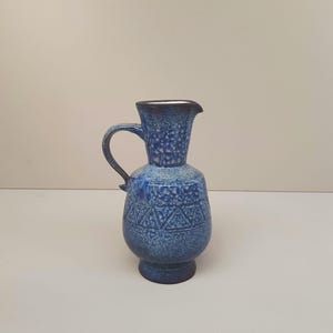 May include: A blue ceramic pitcher with a textured surface and a geometric pattern. The pitcher has a wide mouth and a handle.