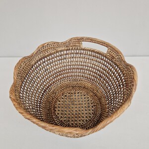 May include: A woven wicker basket with a scalloped edge and a handle. The basket is made of natural brown rattan.