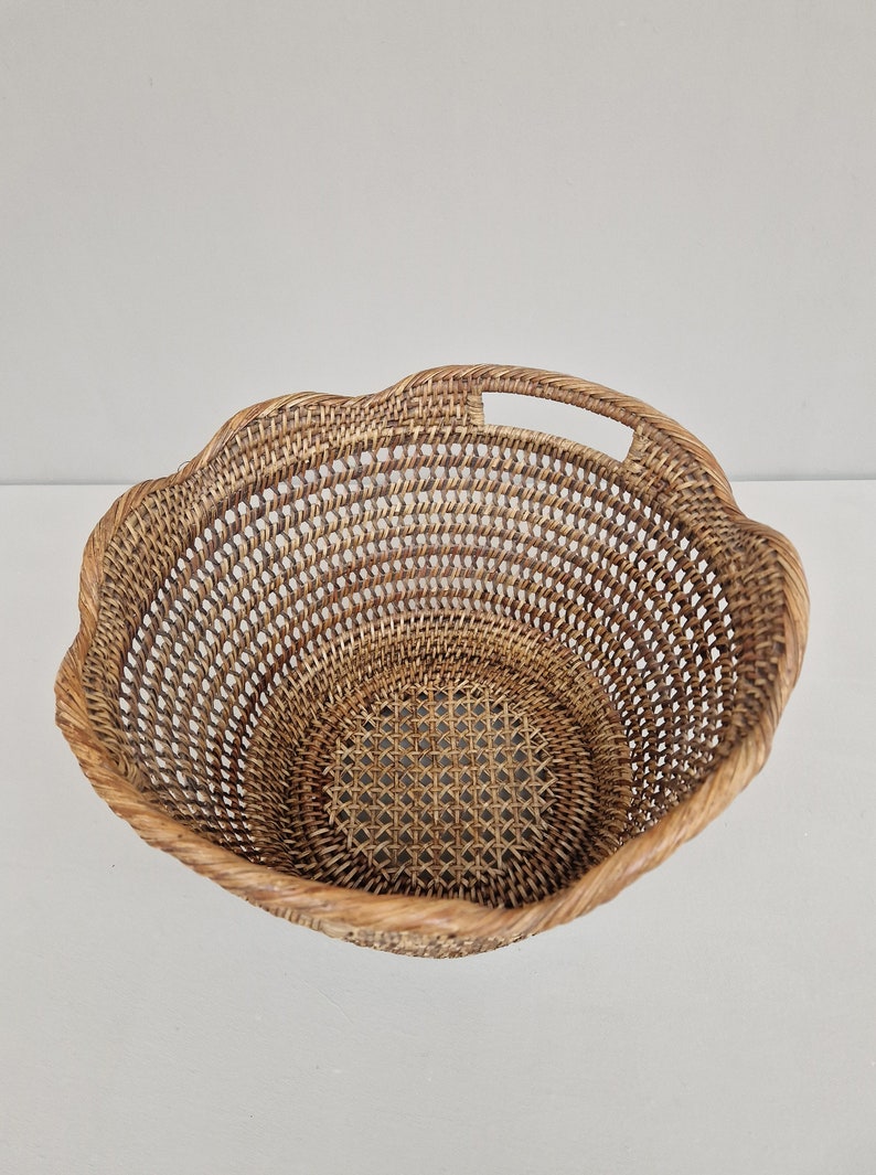 May include: A woven wicker basket with a scalloped edge and a handle. The basket is made of natural brown rattan.
