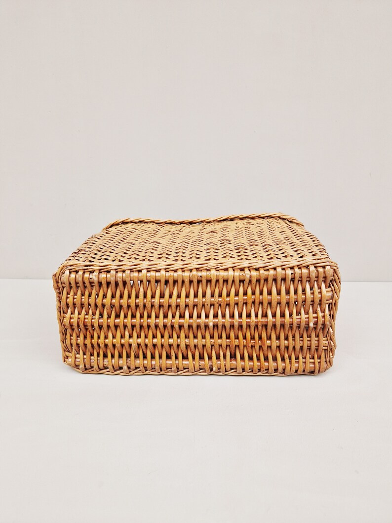 May include: A woven wicker basket with a rectangular shape. The basket is made of natural brown wicker and has a smooth, even weave.