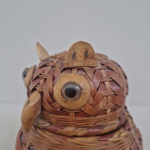 May include: A woven wicker owl figurine with large, round, black eyes. The owl is made of natural brown and tan wicker and has a textured surface.