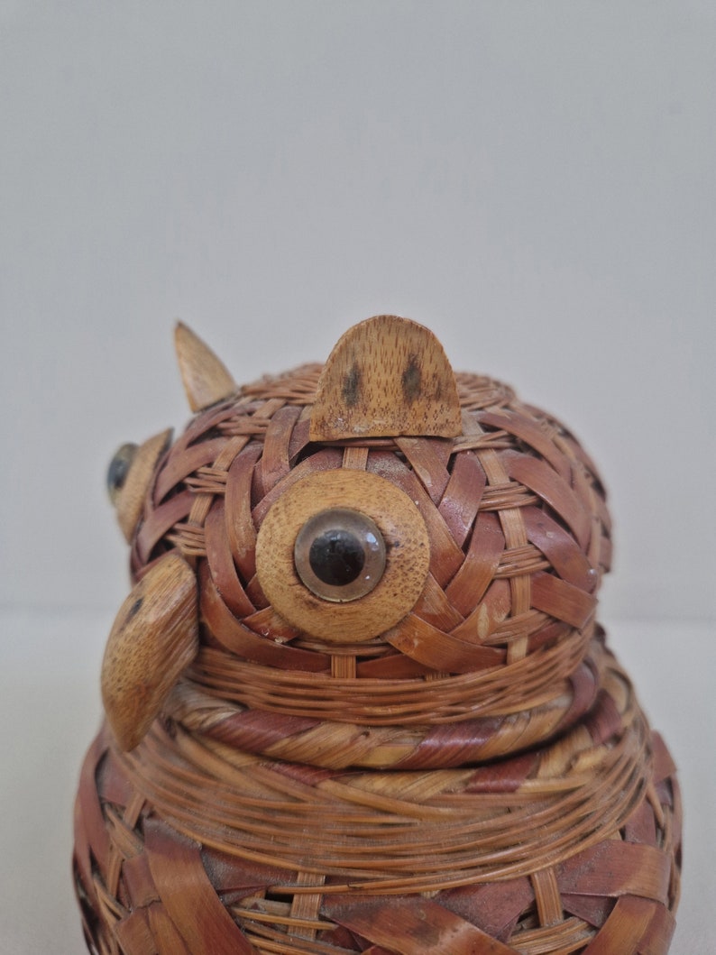 May include: A woven wicker owl figurine with large, round, black eyes. The owl is made of natural brown and tan wicker and has a textured surface.