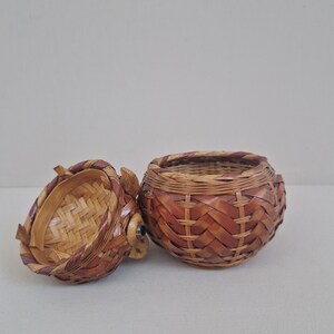 May include: A woven wicker basket with a lid, the lid is open and the basket is brown with a reddish-brown trim.