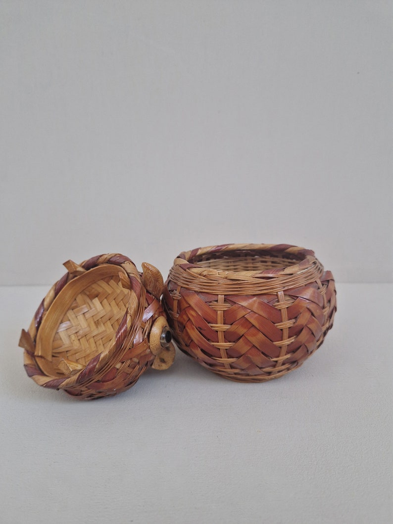 May include: A woven wicker basket with a lid, the lid is open and the basket is brown with a reddish-brown trim.