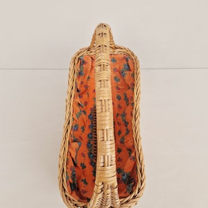 May include: A woven wicker basket with a handle and a floral patterned fabric lining. The basket is empty.