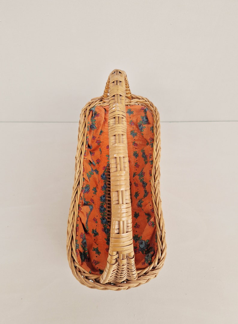 May include: A woven wicker basket with a handle and a floral patterned fabric lining. The basket is empty.