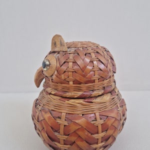 May include: A woven wicker owl-shaped container with a brown and tan color scheme. The owl has a small wooden beak and black eyes.